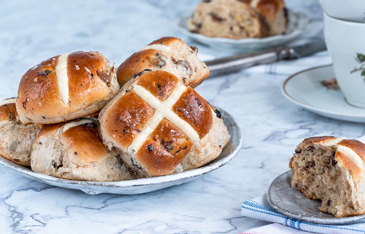 Six hot cross buns stacked up on a plate on a marble table top